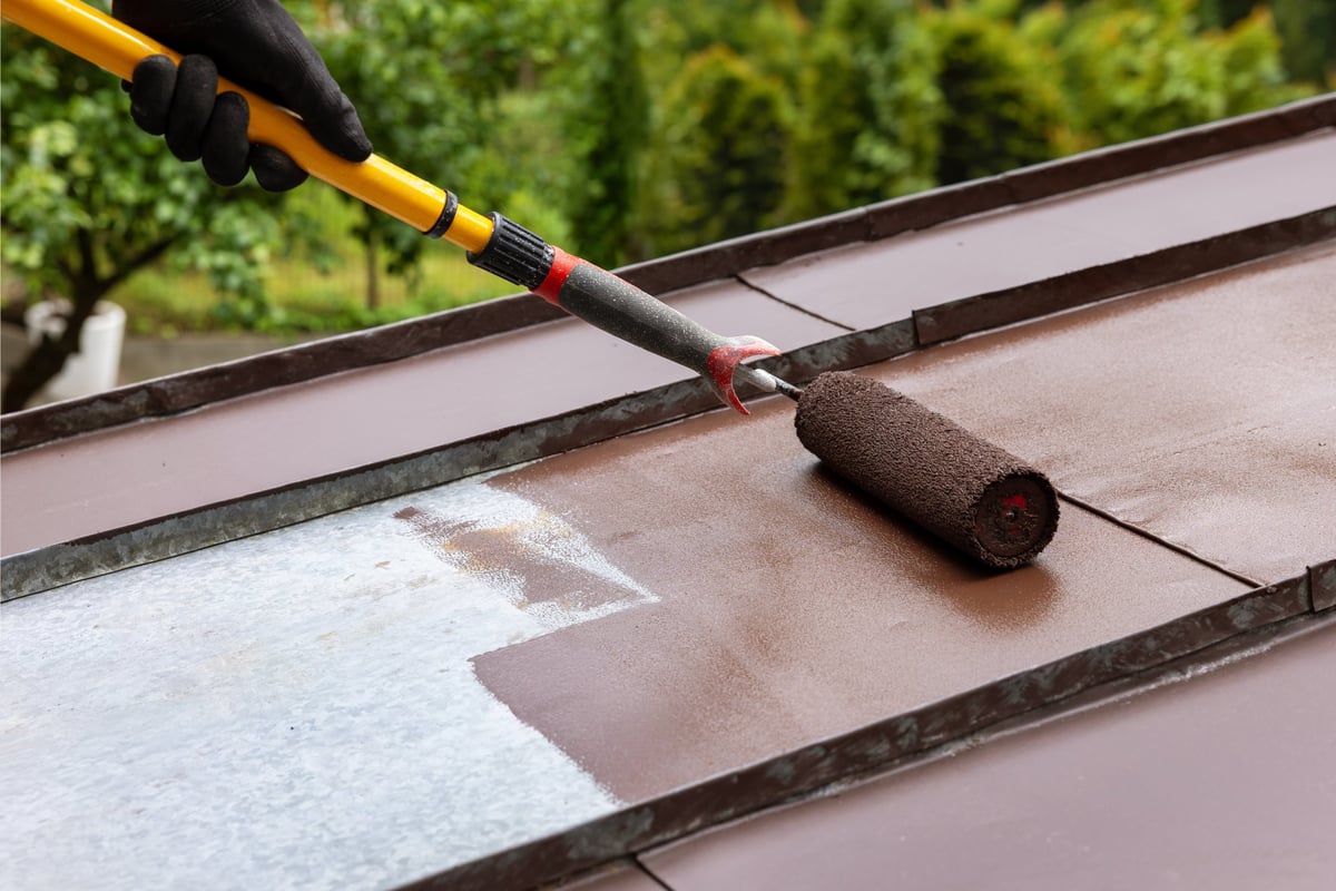 Aplicador con uniforme AislaTherm PRO pintando un techo de lámina con rodillo