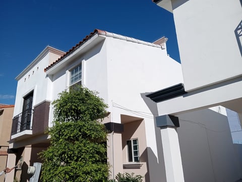 Modern two-story white house with brown accents, green ivy climbing the facade, and clear blue sky in background