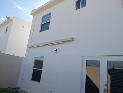 White two-story modern house with multiple windows, glass patio doors, and metal railings under blue sky