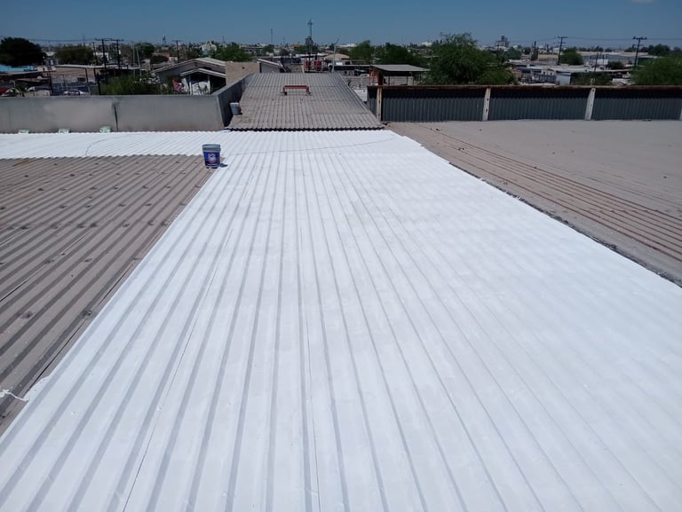 White corrugated metal roof with newly applied coating, extending across an industrial building with adjacent structures visible in the background
