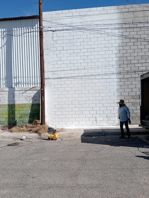 Worker in blue shirt standing near industrial equipment outside white brick building on paved ground