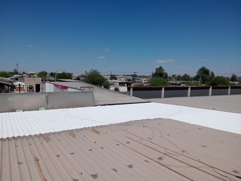 Industrial rooftop with white and tan metal panels under clear blue sky, showing wiring and construction in progress