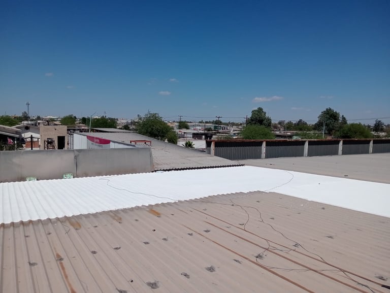 Industrial rooftop with white and tan metal panels under clear blue sky, showing wiring and construction in progress