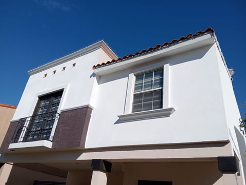 Modern white two-story house with dark tile roof and large windows against clear blue sky