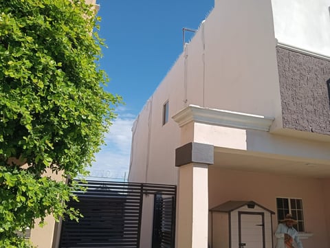 Modern two-story beige house with metal gate and lush green ivy-covered fence on clear day