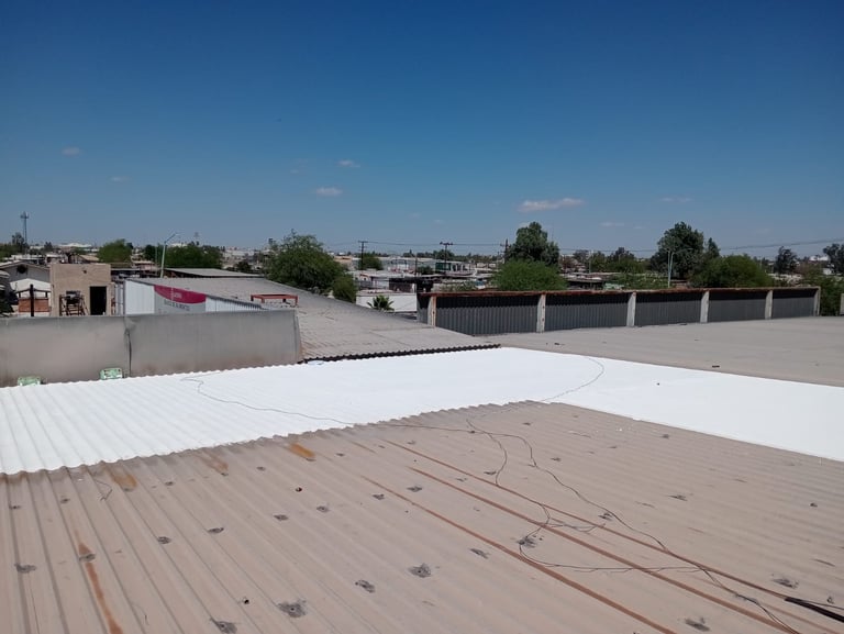 Commercial flat roof under construction or renovation with white membrane covering and exposed substrate, industrial area visible in background