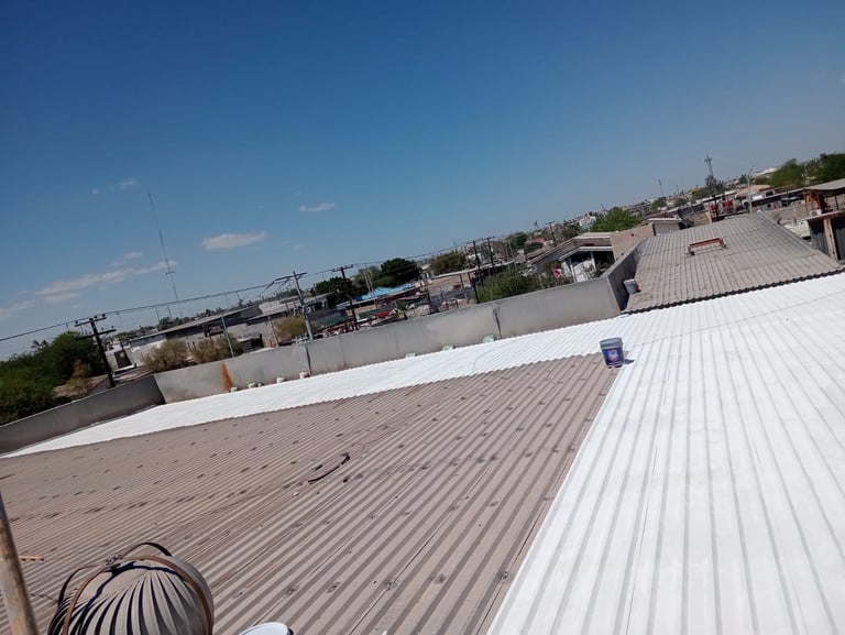 Aerial view of industrial rooftops with corrugated metal panels and surrounding warehouses under clear blue sky